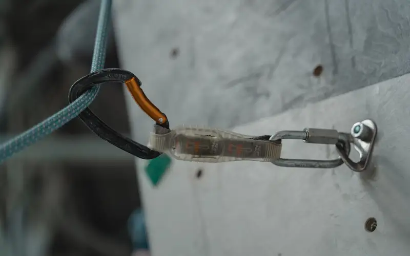 Anclaje metálico con cuerda y mosquetón fijado a una pared