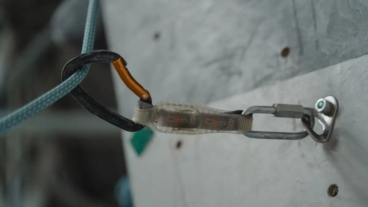 Anclaje metálico con cuerda y mosquetón fijado a una pared