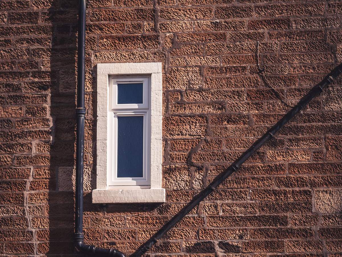 Bajante de pluviales recorriendo una fachada de ladrillo junto a una ventana