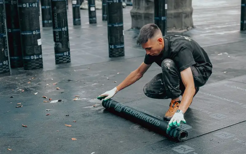 Técnico aplicando una lámina impermeable sobre una cubierta plana