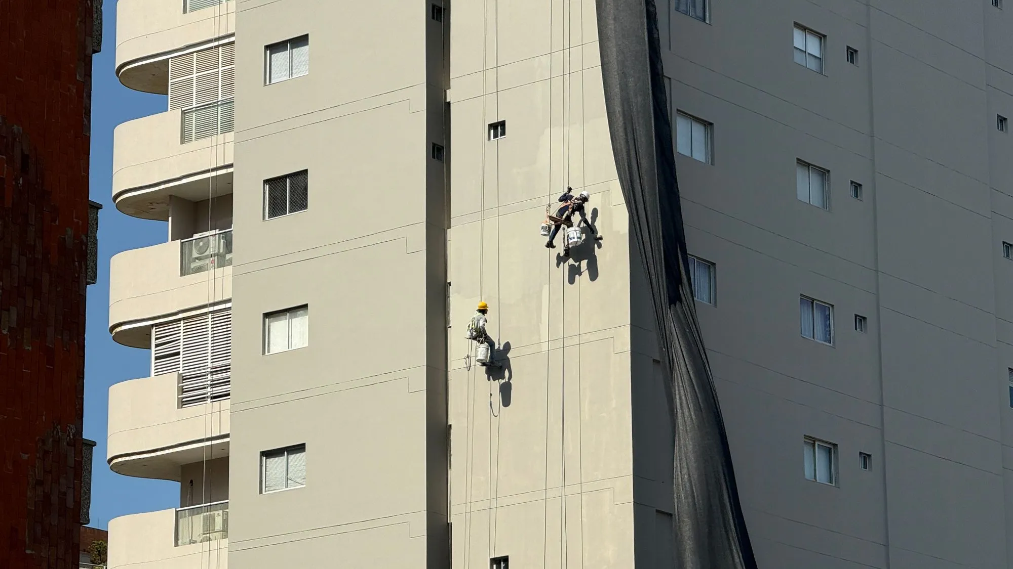 Dos técnicos descolgándose con cuerdas por la fachada de un edificio alto