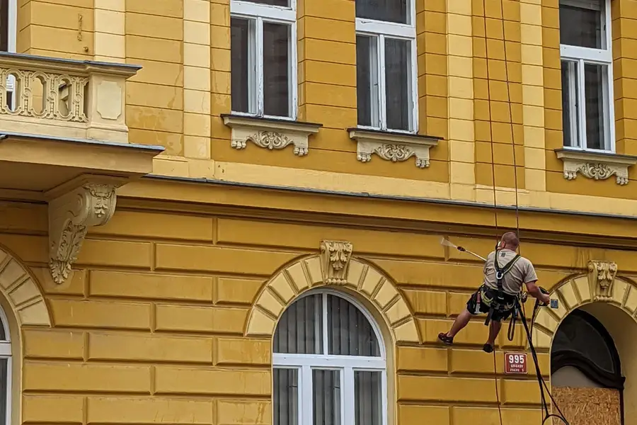 Técnico de trabajos verticales suspendido con cuerdas reparando la fachada de un edificio residencial