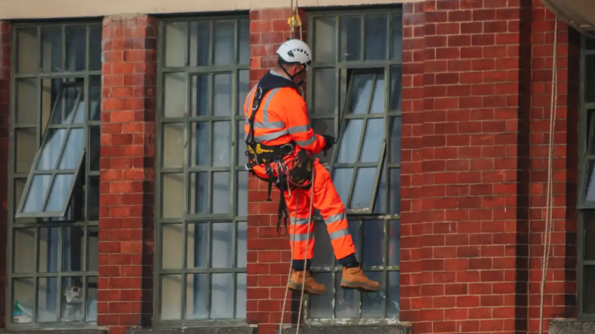 Técnico de trabajos verticales descolgado por cuerdas frente a la fachada de ladrillo de un edificio