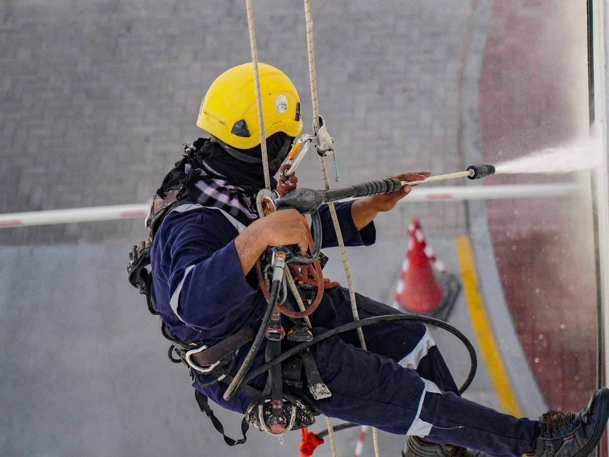 Técnico con casco suspendido con cuerdas limpiando una fachada con agua a presión