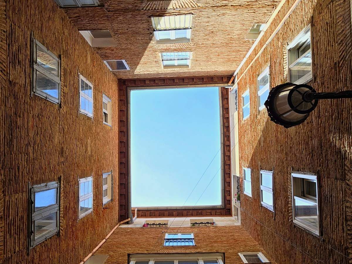 Patio interior de un edificio de ladrillo visto desde abajo, con ventanas en todos los paños