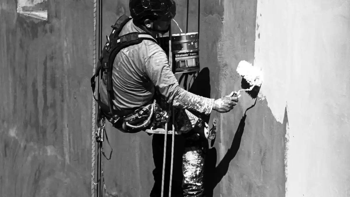 Técnico de trabajos verticales pintando una fachada suspendido con cuerdas