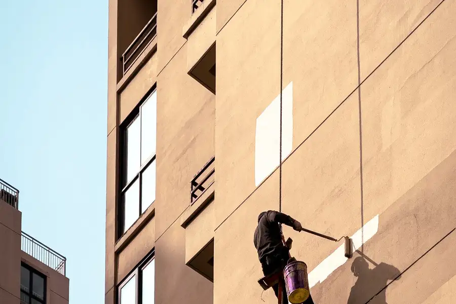 Técnico suspendido con cuerdas pintando la fachada de un edificio alto