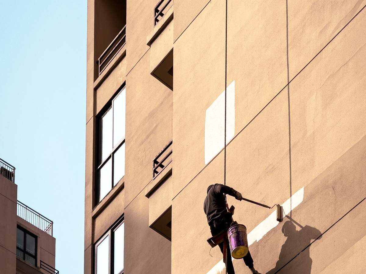 Técnico suspendido con cuerdas pintando la fachada de un edificio alto