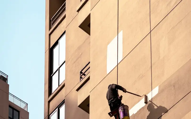 Técnico suspendido con cuerdas pintando la fachada de un edificio