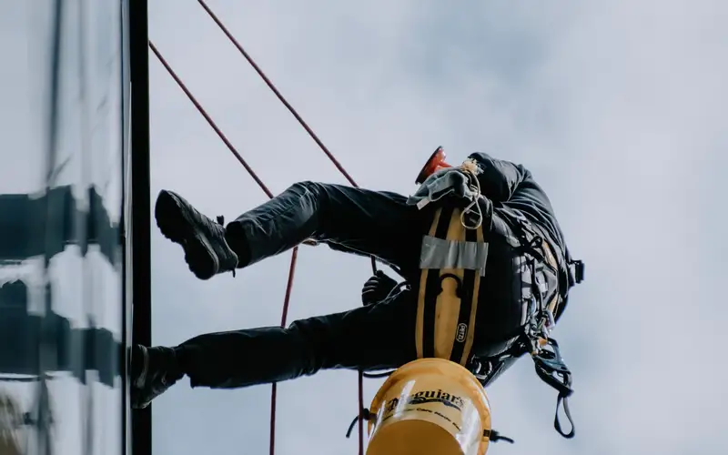 Técnico de trabajos verticales descolgado junto a una ventana de un edificio